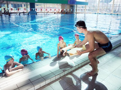 Trener tłumaczy dzieciom technikę pływania. Dzieci są w wodzie.